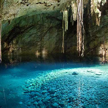Ein türkisfarbenes Wasserbecken leuchtet in einer Höhle.